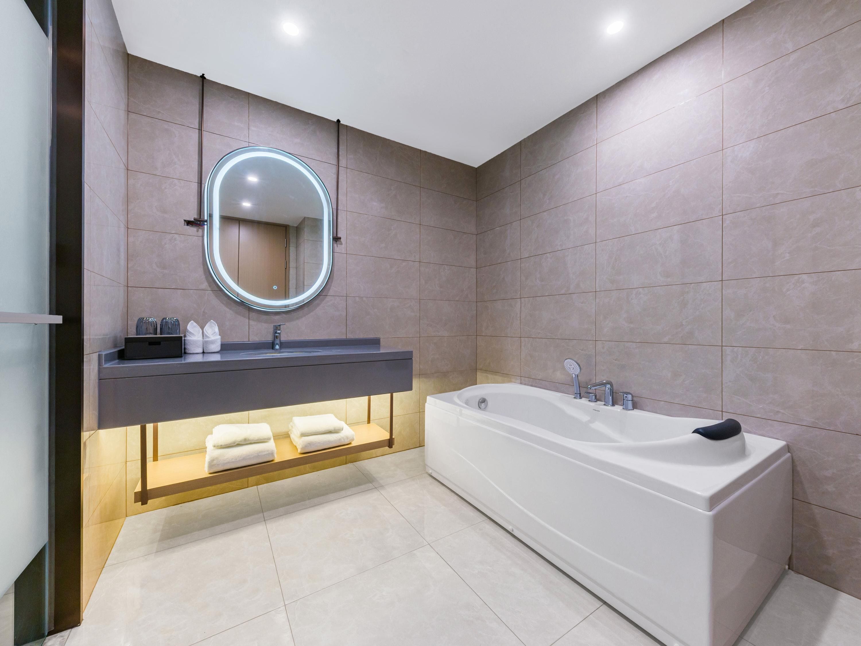 A modern bathroom with a large bathtub, a vanity with a mirror, and a shelf with towels.