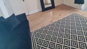 A room with a patterned rug, a dark-colored sofa, a white door, and a mirror on the wall. - Beautiful 1-bed Apartment in North London (London)