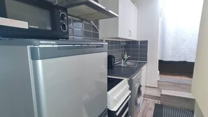A compact kitchen with a stainless steel refrigerator, a microwave, and a built-in oven. The kitchen has a tiled backsplash and a small window with a curtain. - Beautiful 1-bed Apartment in North London (London)