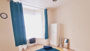 A bedroom with a bed, a chair, a wardrobe, and a window with curtains. - Beautiful 1-bed Apartment in North London (London)