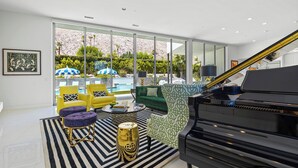 A modern living room with a grand piano, a pool, and outdoor seating. - Cosmopolitan - Walk to Palm Canyon! (Palm Springs)