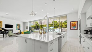 A modern kitchen with a large island, white cabinetry, and a view of a pool and mountains. - Cosmopolitan - Walk to Palm Canyon! (Palm Springs)