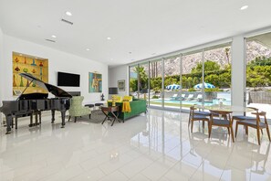 Amplio salón con un piano de cola, un sofá verde y vista a la piscina.