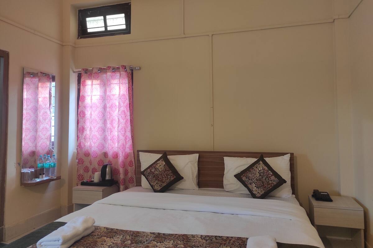 A hotel room with a bed, a nightstand, a telephone, and a window with curtains.