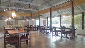A spacious dining area with wooden tables and chairs, hanging lights, and a high ceiling with metal beams. - Jironi Resort (Raha Circle)