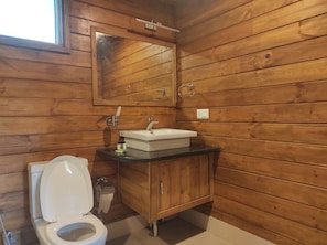 Bany d'una cabana de fusta amb vàter, banyera i mirall.