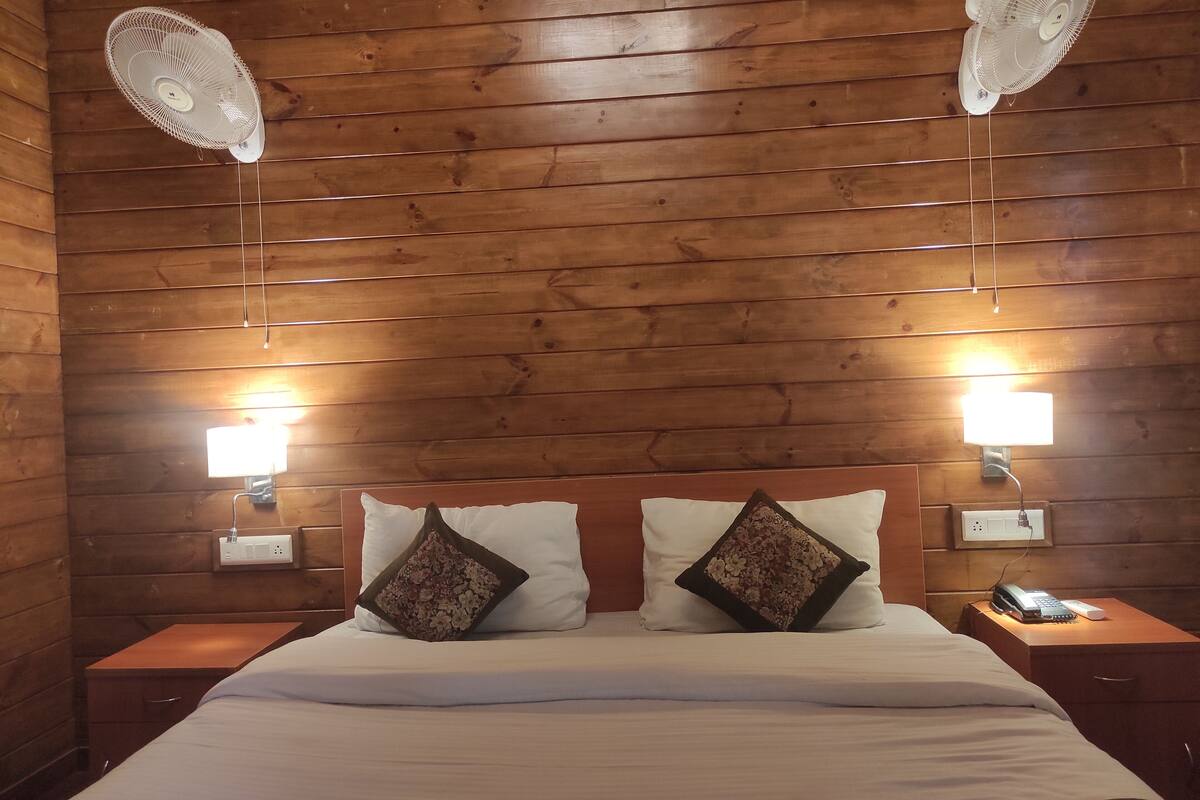 A wooden-paneled room with a bed, two wall-mounted fans, and bedside lamps.