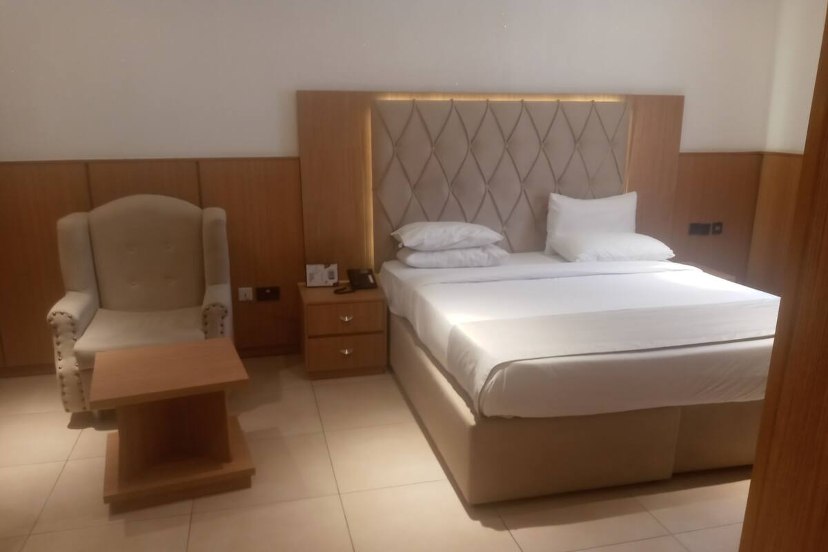 A hotel room with a large bed, a chair, a nightstand, and a small table.