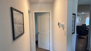 Un pasillo con una fotografía enmarcada a la izquierda, una puerta blanca al final y un termostato en la pared.