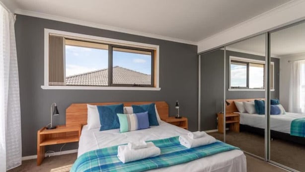 A bedroom with a large bed, a nightstand, a mirror, and a window. - Mountain Explorer - 2BR Farmland View Retreat (Deloraine)