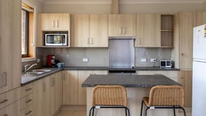 A modern kitchen with light wood cabinets, a central island with two chairs, a microwave, a stove, and a refrigerator. - Mountain Explorer - 2BR Farmland View Retreat (Deloraine)