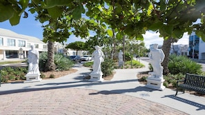 Un chemin pavé bordé de statues blanches, entouré de verdure et avec des bâtiments en arrière-plan.