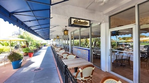 An outdoor patio area with tables and chairs, a covered section, and a view of the street.