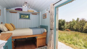 A cozy room with a bed, a window, and a view of the outdoors. - Two Moors Shepherds Hut (Exeter)