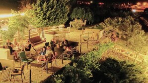 Zona d'estar a l'aire lliure amb taules i cadires, envoltada d'arbres i vegetació.