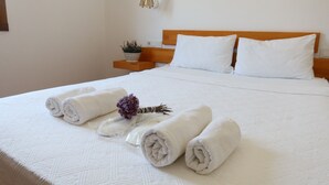 Un llit ben fet amb tovalloles blanques arremolinades i una flor morada decorativa.