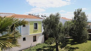 Edifici de dues plantes amb teulada de rajola, un petit jardí d'oliveres i un cel blau clar.