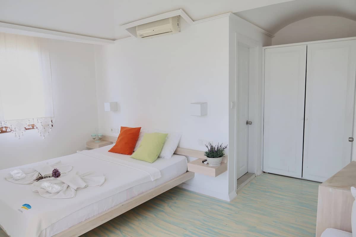 A minimalist bedroom with a bed, a bedside table, a nightstand, a wardrobe, and a small potted plant.