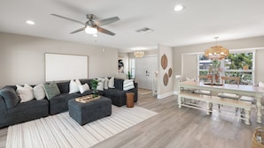 Una sala de estar moderna con un sofá seccional gris, una mesa de centro y un comedor con una mesa de madera y bancos.
