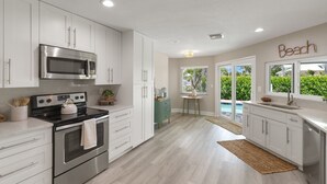 Una cocina moderna con armarios blancos, electrodomésticos de acero inoxidable y vistas a una piscina a través de puertas corredizas de vidrio.