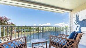 A balcony with two wooden chairs and a small table, overlooking a body of water and a landscaped garden. - Lake View ~ Bayside Gated Resort ~ 2 Golf Carts (Miramar Beach)