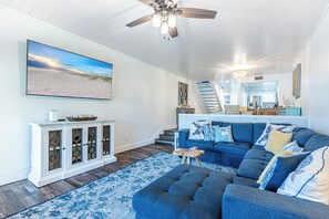 Een ruime woonkamer met een grote modulaire bank, een houten kast en een trap naar een hoger niveau.