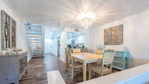 A modern kitchen with white cabinets, a dining area with a wooden table and chairs, and a staircase leading to another level. - Lake View ~ Bayside Gated Resort ~ 2 Golf Carts (Miramar Beach)