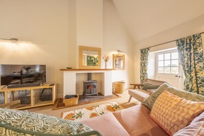 A cozy living room with a television, a fireplace, a sofa, and a window with curtains.