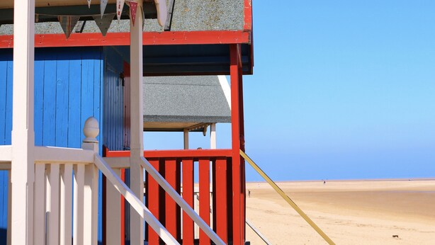 Une maison de plage à l’extérieur rouge et bleu, dotée d’un balcon et offrant une vue sur la plage.