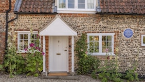Une maison en pierre avec une porte blanche, un petit porche et une plaque fixée au mur.