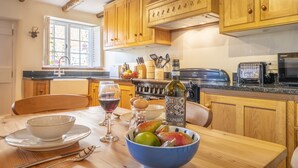 Une cuisine avec des meubles de rangement en bois, une table à manger avec un saladier de fruits, des verres à vin et une bouteille de vin.