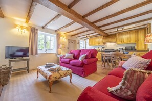 A cozy living room with a wooden ceiling, a television, a red sofa, and a kitchen in the background.