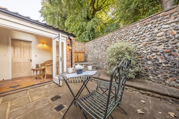 Relax in this serene outdoor seating area with a metal table and chairs, a small table and chair, and a door leading to the interior.