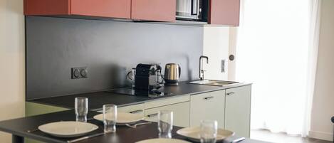 Uma cozinha moderna com bancada preta, armários vermelhos e micro-ondas. Há pratos e copos na mesa, e um café está visível.