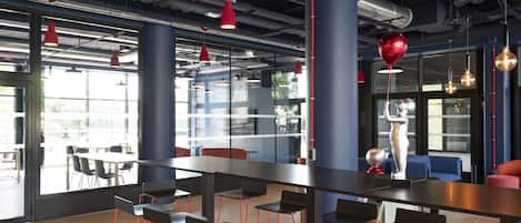 Un moderno comedor con mesas y sillas altas, ventanas amplias e iluminación colgante roja.