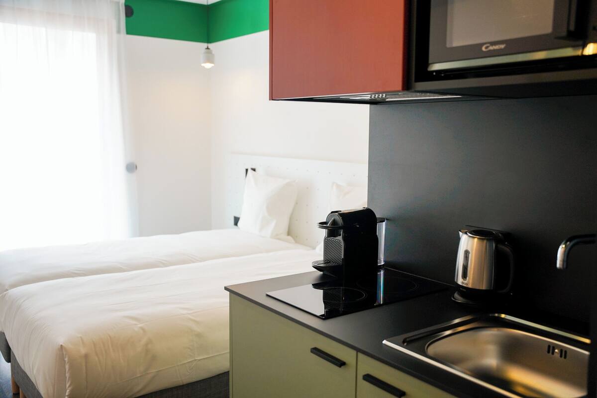 Hotellihuone, jossa on sänky, pieni keittiönurkkaus, jossa on kahvinkeitin, ja mikroaaltouuni.