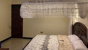 A bedroom with a bed, a wooden door, and a ceiling light fixture. - Joyce Hotel (Mubende)