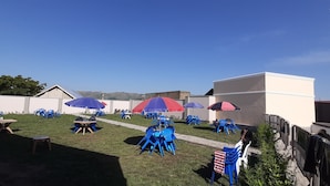 An outdoor seating area with blue and red umbrellas, tables, and chairs. - Joyce Hotel (Mubende)