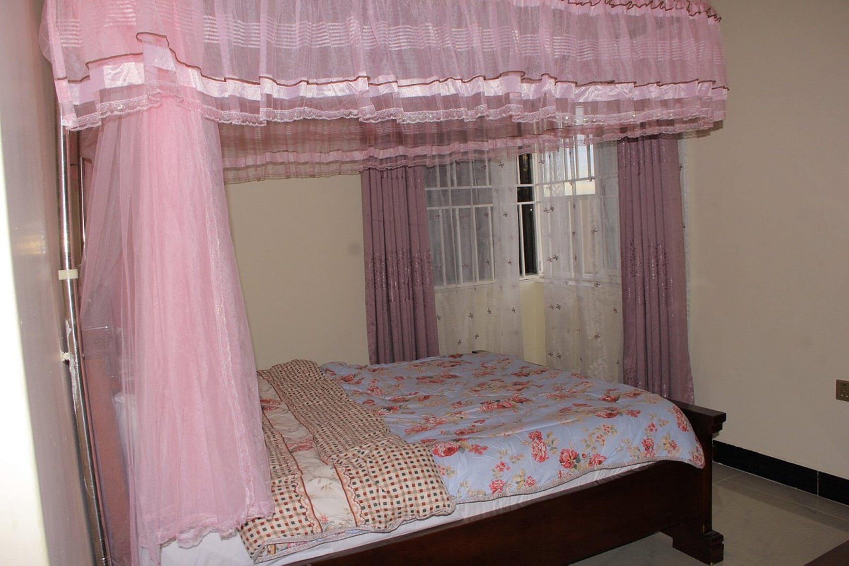 Ein Schlafzimmer mit einem Himmelbett, floralem Bettzeug und transparenten Vorhängen.