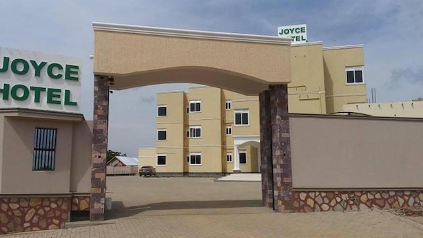 The entrance to Joyce Hotel with a clear sign, a paved driveway, and a multi-story building in the background. - Joyce Hotel (Mubende)