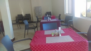 A dining area with checkered red and white tablecloths, black chairs, and a window providing natural light. - Joyce Hotel (Mubende)
