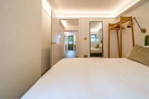Habitación de hotel con una cama grande, una escalera de madera, un espejo y vista a un pasillo.