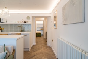 A modern kitchen with a central island, a dining area with a table, and a hallway leading to a bedroom. - ✨ Contemporary Cotswold Pad – Heart of Stow-on-the-Wold (Stow-on-the-Wold)