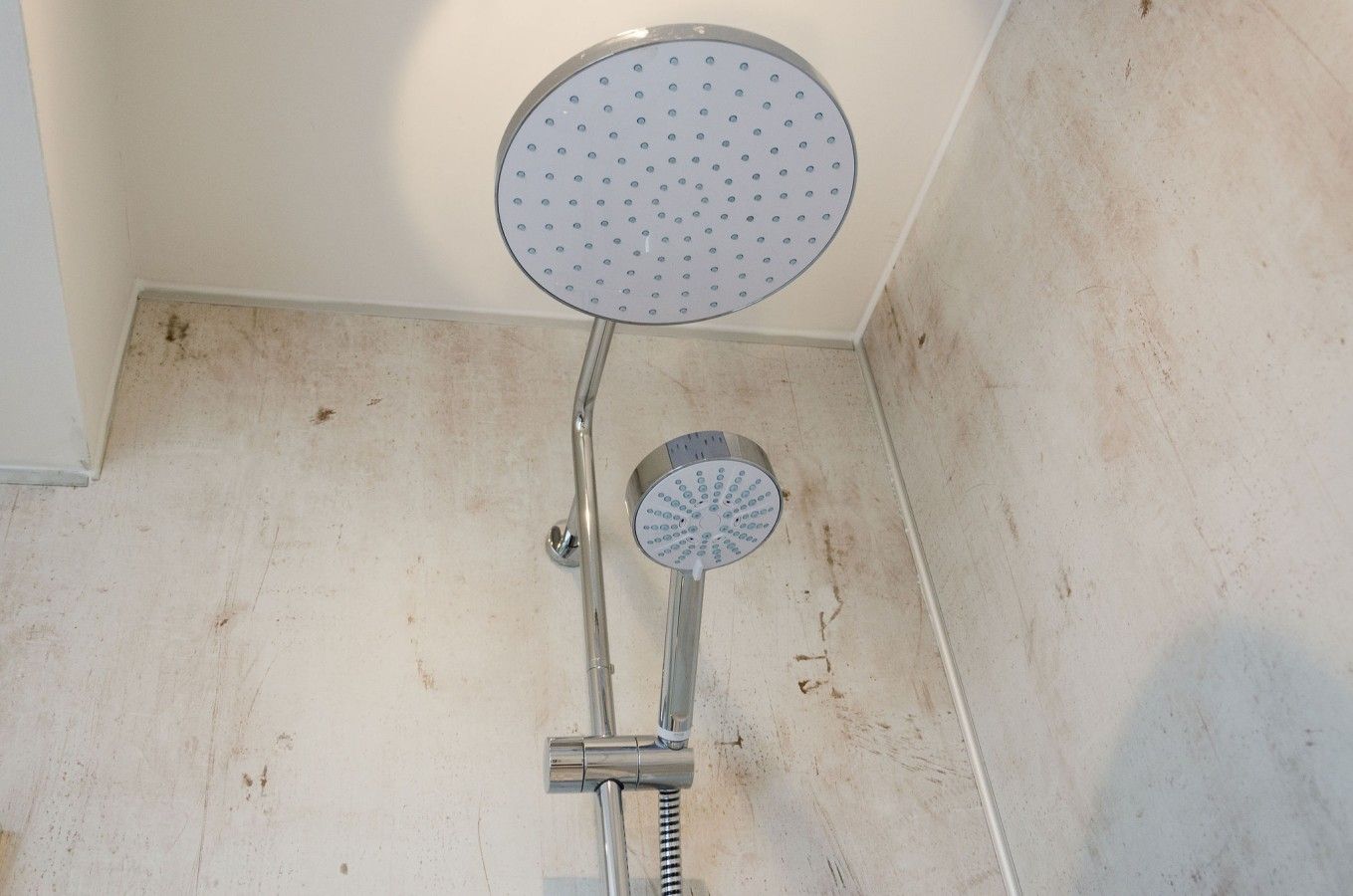 Une douche équipée d’un pommeau de douche rond et d’un pommeau de douche à main fixé sur un accessoire chromé.