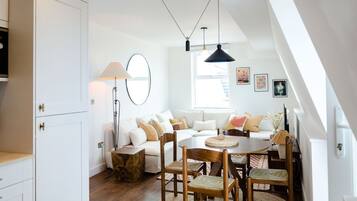 A modern living space with a dining area, sofa set, and a kitchen with white cabinetry.
