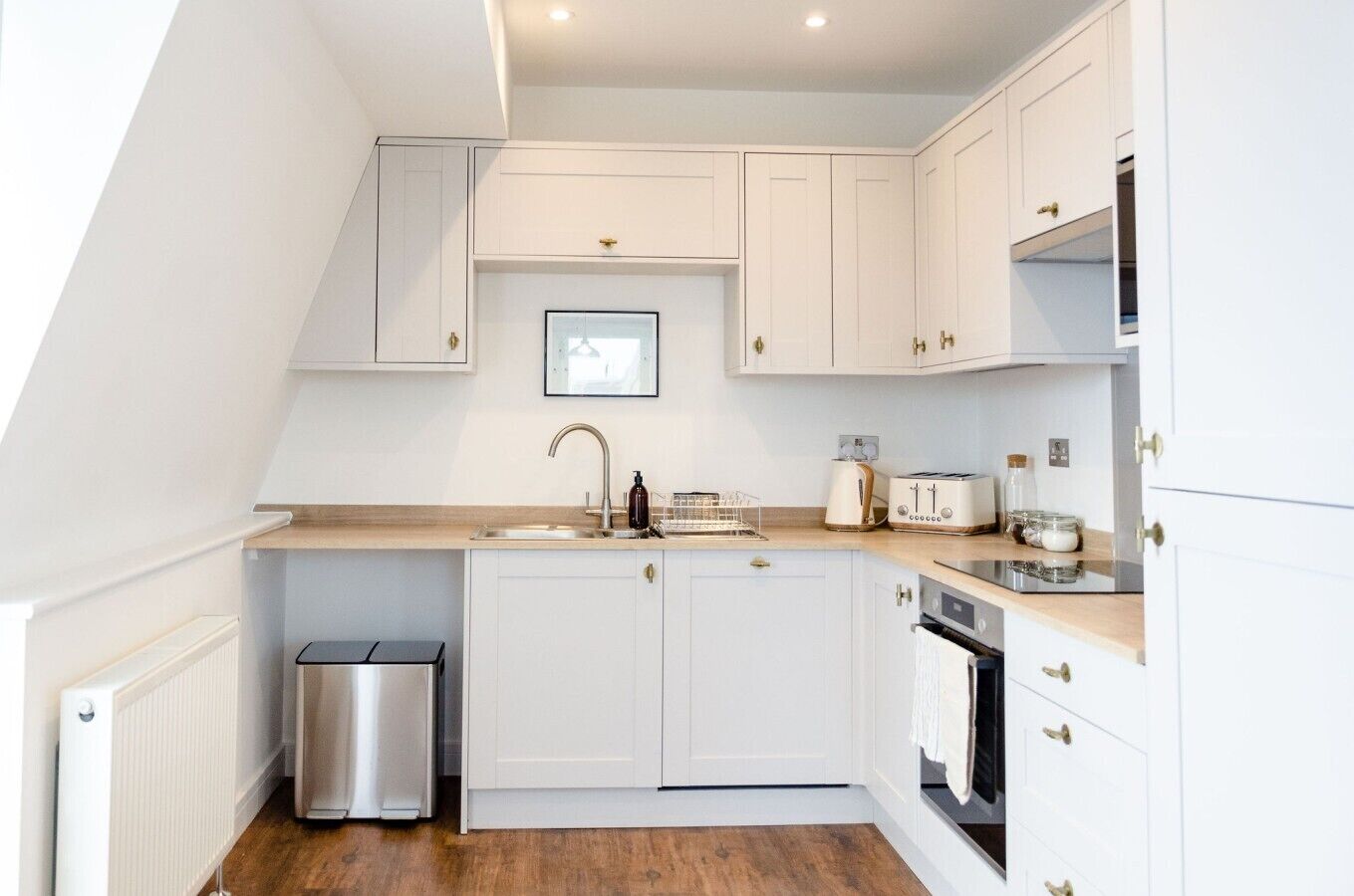 A modern kitchen with white cabinetry, a stainless steel sink, a toaster, and a small trash bin.