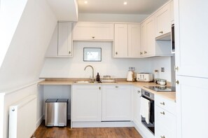 A modern kitchen with white cabinetry, a stainless steel sink, a toaster, and a small trash bin.