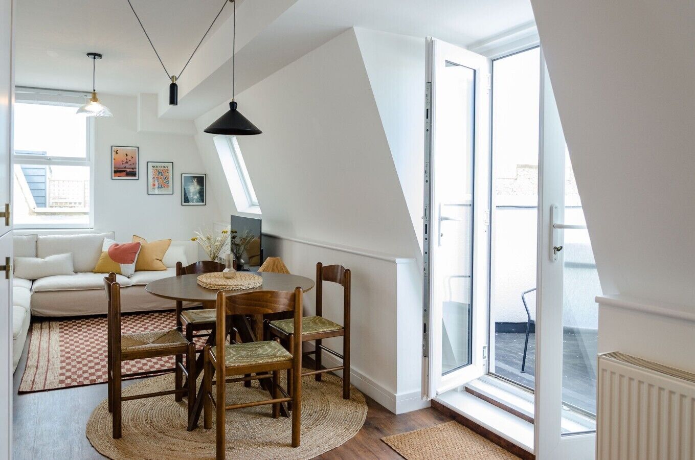 A modern loft apartment with a dining area, a sofa, and a large window providing natural light.