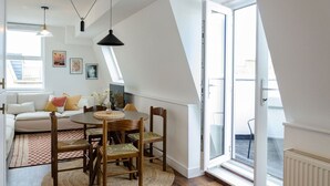 A modern loft apartment with a dining area, a sofa, and a large window providing natural light.