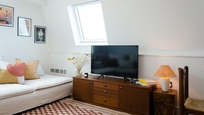 Ett sovrum med en sÀng, en tv pÄ en byrÄ i trÀ, ett fönster och en lampa.